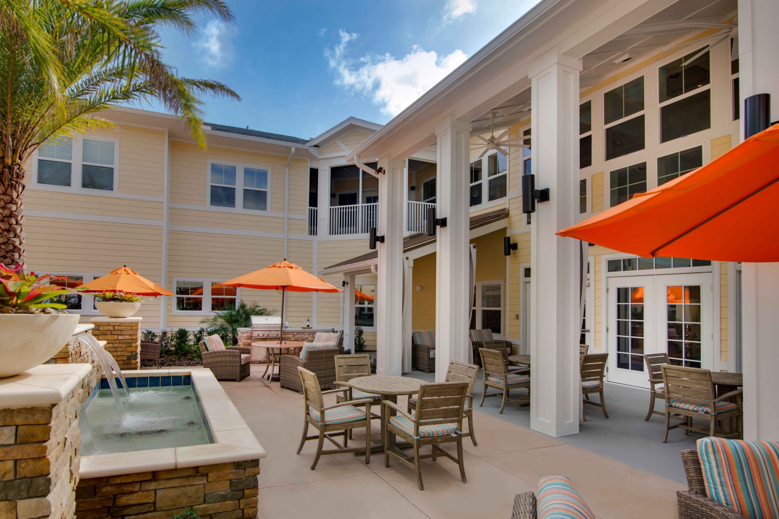 Sonata West 2010 - The Summit of Winter Garden An outdoor patio with wicker furniture, umbrellas, and a water feature at The Summit of Winter Garden, a senior living community near Clermont, FL.