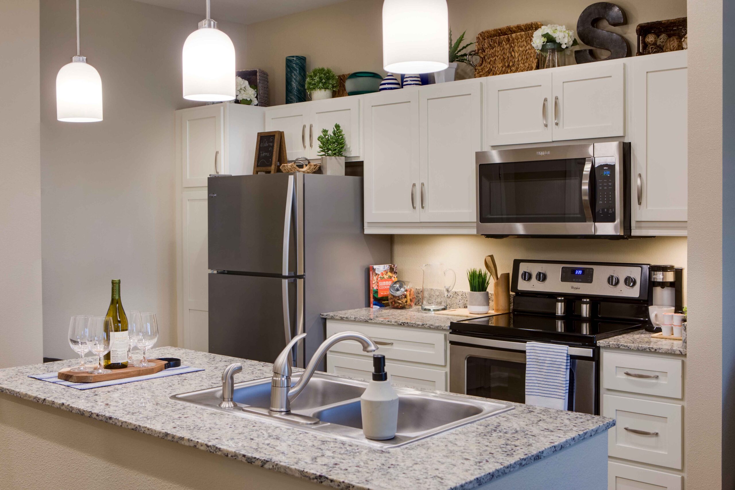 Sonata West 2035 - The Summit of Winter Garden A kitchen with marbled counters, a kitchen island, white cupboards, a fridge, a microwave, and a stove at The Summit of Winter Garden, a senior living community near Clermont, FL.